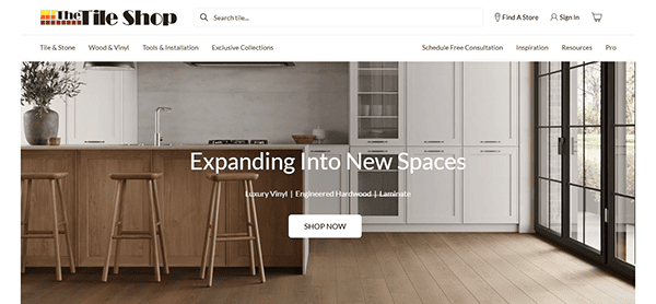 A modern kitchen with wood flooring, white cabinets, wooden stools, and text overlay that reads, “Expanding Into New Spaces. Luxury Vinyl | Engineered Hardwood | Laminate.” Perfect inspiration for tile design lovers browsing the best tile websites.