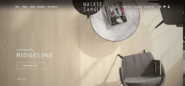 A modern interior with light wood flooring, a round marble table with magazines, and a gray chair. Text on screen reads "Latest Collection Ridgeline. Explore Now." Discover tile design inspiration on one of the best tile websites, Walker Zanger.