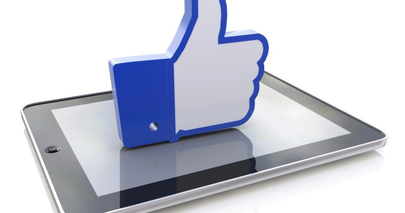 A 3D blue and white thumbs-up "like" icon stands upright on the screen of a tablet device, symbolizing social media approval or positive feedback.