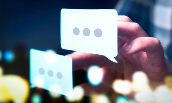 A hand interacts with two digital speech bubbles, each containing three dots, symbolizing texting or online messaging with blurred lights in the background—perfect for showcasing WordPress multilingual content or plugins.