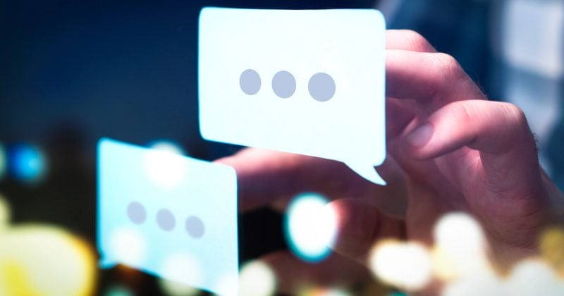 A hand interacts with two digital speech bubbles, each containing three dots, symbolizing texting or online messaging with blurred lights in the background—perfect for showcasing WordPress multilingual content or plugins.