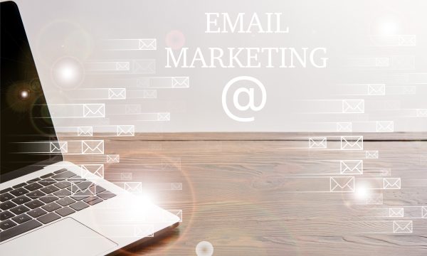 A laptop on a wooden desk with digital envelope icons and the words "Email Marketing" displayed in the background.