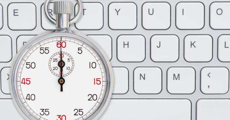 A silver stopwatch displaying 10 seconds is placed on a white computer keyboard.