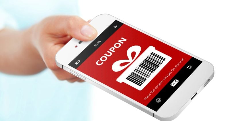 A hand holds a smartphone displaying a digital coupon with a barcode and a gift icon on the screen.