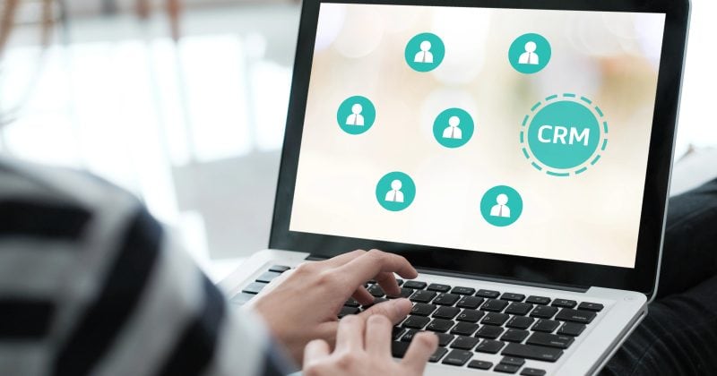 Person using a laptop displaying a CRM software interface with icons representing connected users.