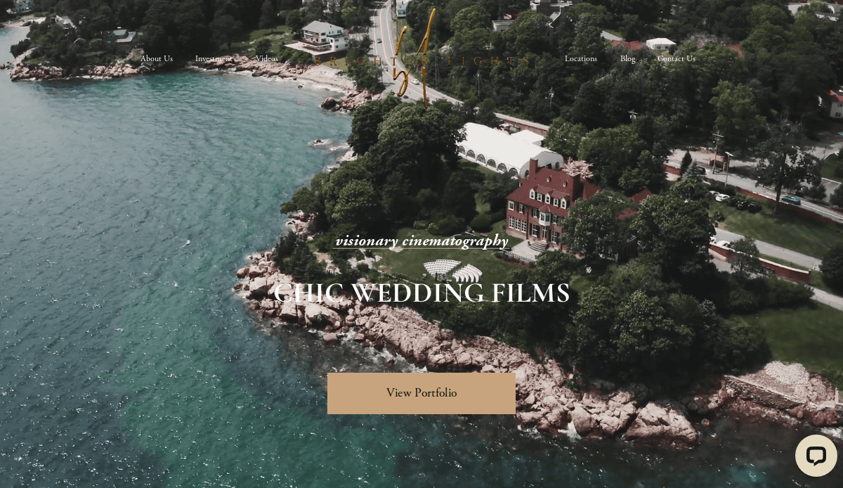 Aerial view of a rocky coastline with green trees, houses, and a large building by the water. Text overlay reads “Visionary cinematography. Chic wedding films.” Perfect inspiration for website designers or your dream wedding website. Button says “View Portfolio.”.