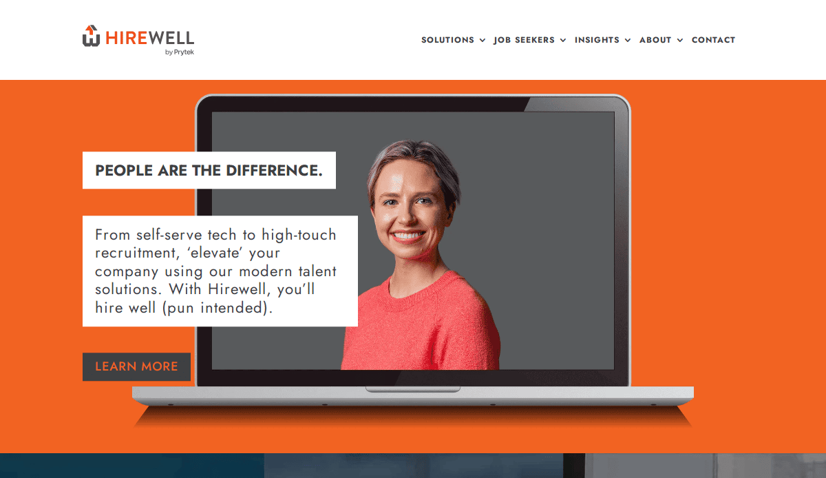 A smiling woman in a pink sweater appears on a laptop screen, set against an orange background. The website design highlights Hirewell’s recruitment agency solutions, with a “Learn More” button inviting visitors to explore further.