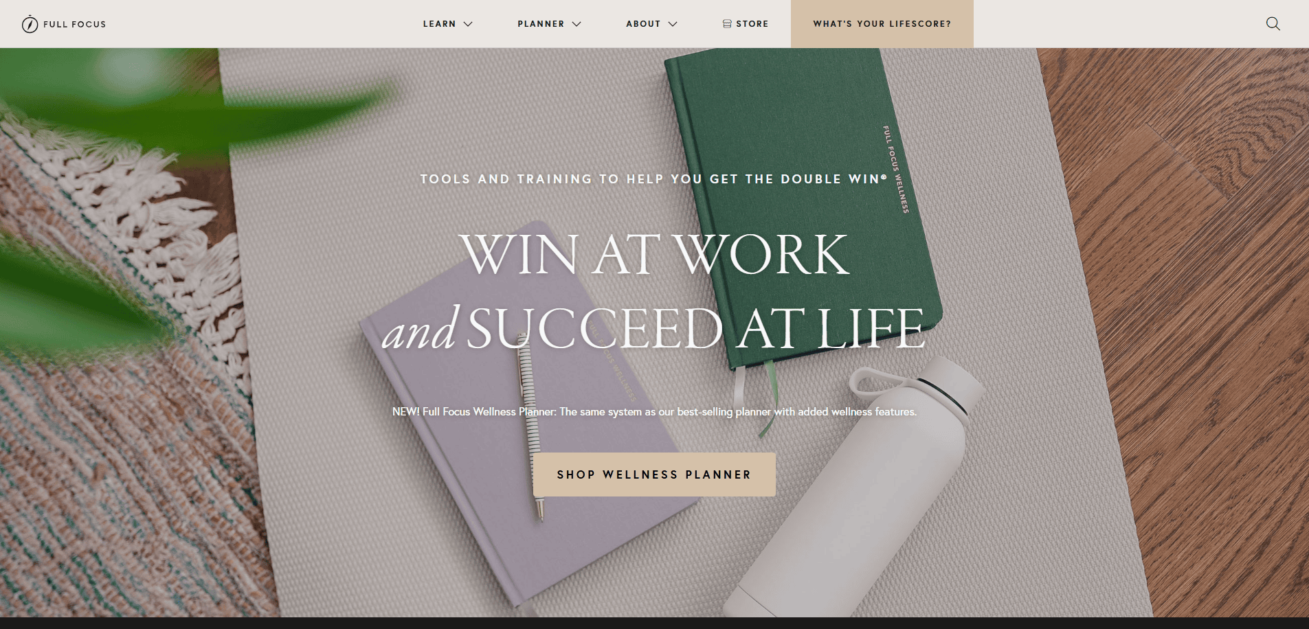 A neatly arranged desktop with two closed notebooks (green and gray), a pen, and part of a plant. The text overlay says, “Win at work and succeed at life,” perfect inspiration for any life coach website. Button: “Shop Wellness Planner.”.