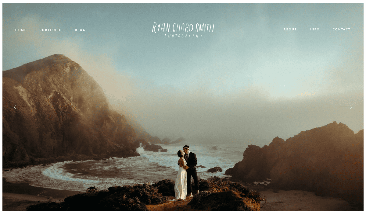 A couple in wedding attire stands on a cliff overlooking the ocean, surrounded by rocky hills and waves at sunset—perfect for wedding website inspiration against a stunning natural backdrop.