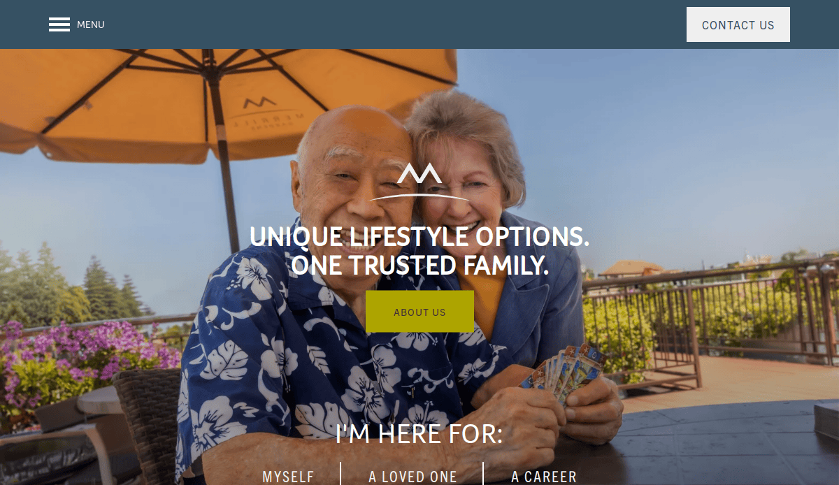 An elderly man and woman sit smiling outdoors under a large umbrella, holding playing cards. Text reads, “Unique lifestyle options. One trusted family.”—showcasing thoughtful senior living website design. A yellow “About Us” button sits below.
