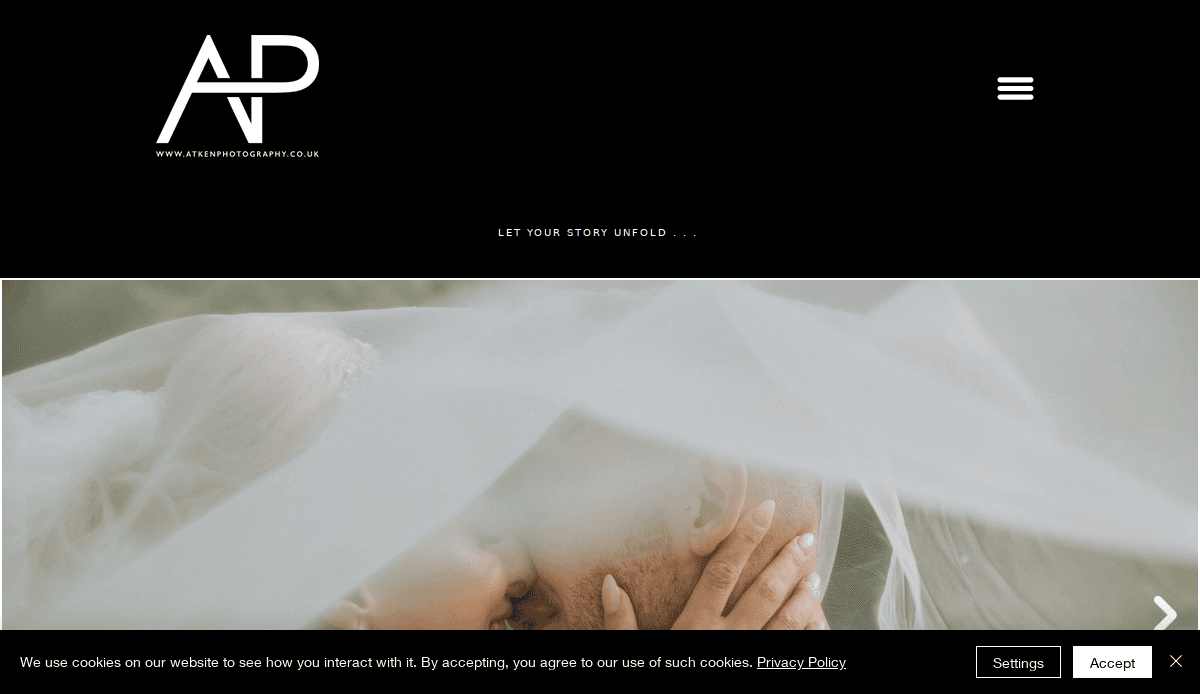 A close-up of a couple embracing and sharing a kiss under a sheer white veil, with soft natural light. At the top, wedding website designers’ branding and navigation appear, while a cookie consent banner is visible at the bottom.