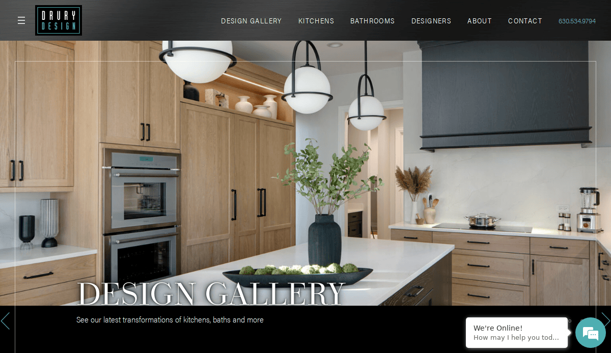 Modern kitchen with light wood cabinets, white countertops, built-in oven, black accents, and a central island decorated with a black vase holding green branches. Perfect inspiration for your next Kitchen Remodeling project. Text reads Design Gallery.