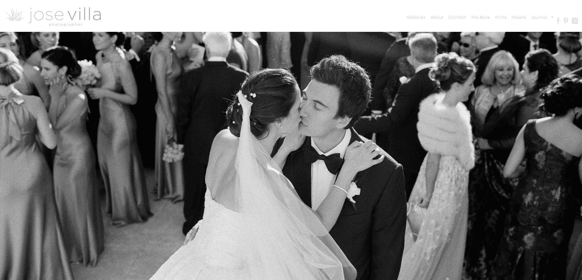 A bride and groom share a kiss in the midst of a lively wedding crowd, with guests socializing and smiling in the background—a perfect moment for wedding website designers to showcase on your custom wedding website. The scene is in black and white.