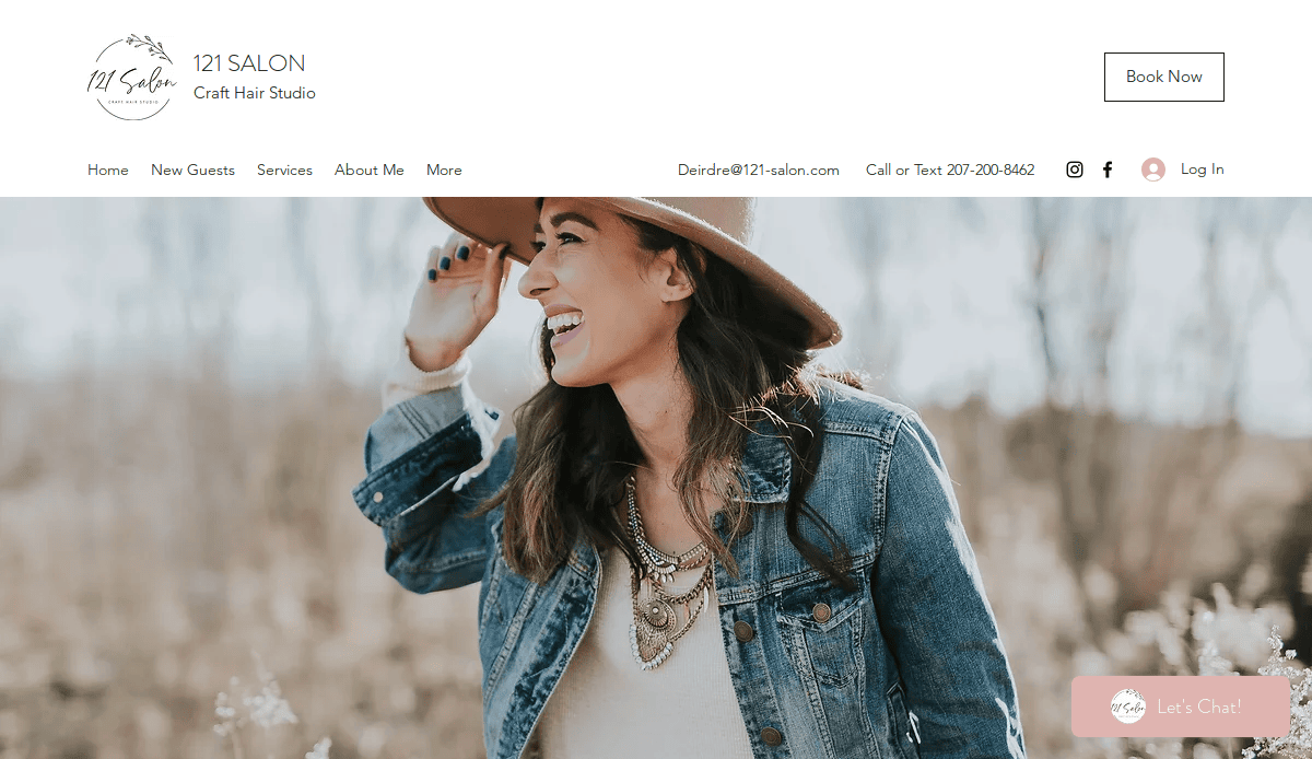 A woman wearing a hat, jean jacket, and layered necklaces smiles and laughs outdoors in a field, with soft natural light and a blurred background. The website header shows “121 Salon” and contact options.