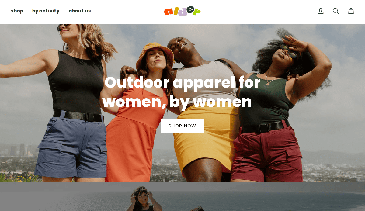 Four women in bright outdoor clothing stand together smiling and posing with arms raised, with a cityscape and blue sky in the background. Text reads Outdoor apparel for women, by women.