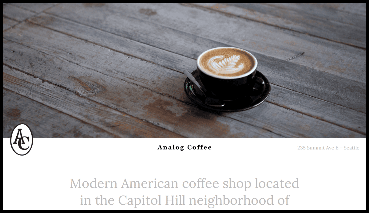 A latte with latte art sits in a black cup and saucer on a rustic wooden table at Analog Coffee, a coffee shop in Seattle’s Capitol Hill neighborhood.