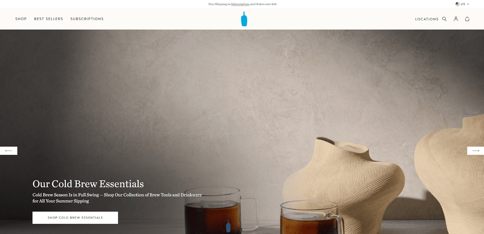 Two glasses of cold brew coffee sit in front of textured beige vases on a neutral background. White text promotes cold brew essentials, with a button to shop the collection on the Blue Bottle Coffee website.