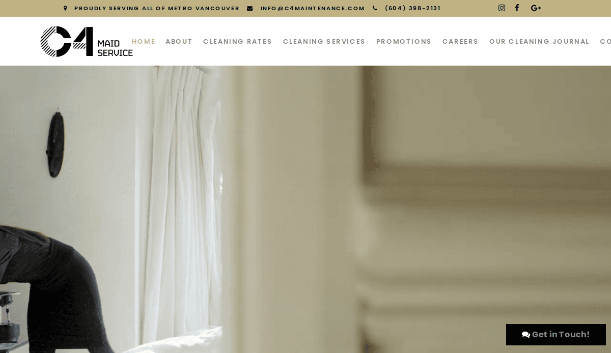 A softly lit room with sheer white curtains hanging by a window. The edge of a bed and part of a persons shoulder are visible on the left side, with a cream-colored wall or door frame in the foreground on the right.