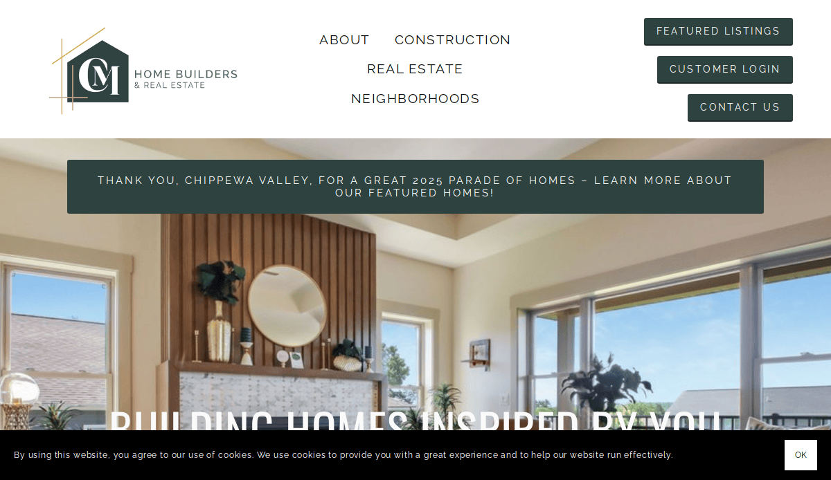 A website homepage for CM Home Builders & Real Estate, featuring a navigation menu, large windows with a scenic outdoor view, and a banner announcing the 2025 Parade of Homes in Chippewa Valley.