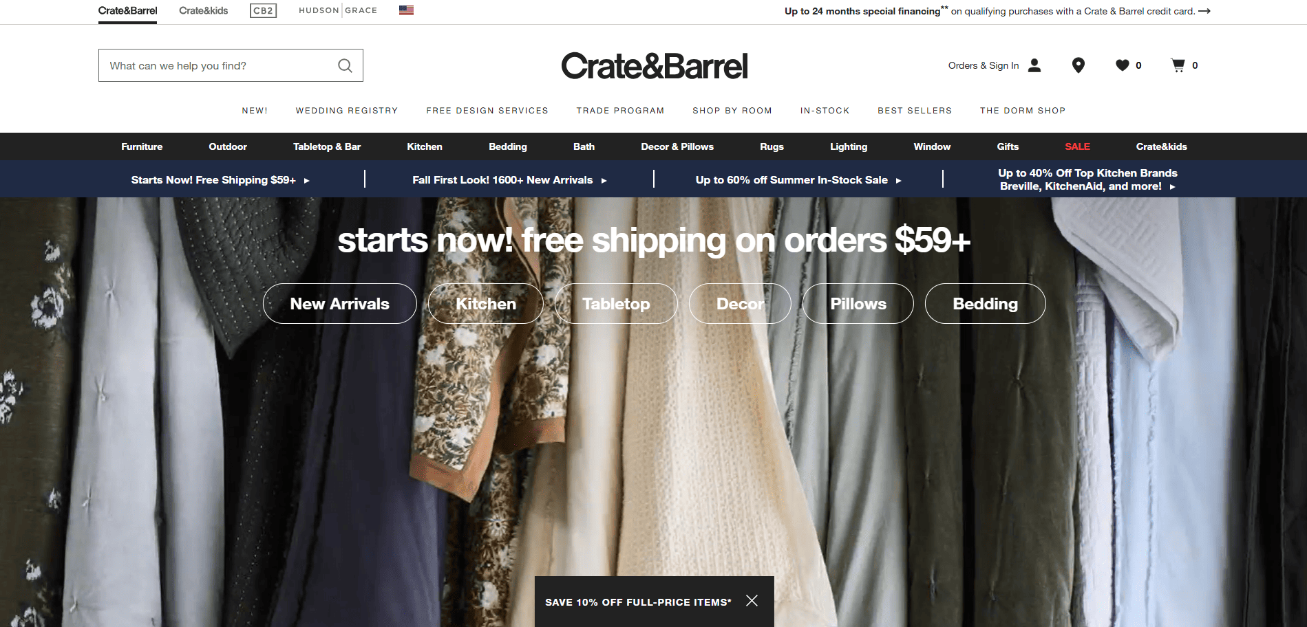 Crate & Barrel homepage featuring a navigation menu, a banner promoting free shipping on orders over $59, and a background image of assorted hanging textiles in various colors and patterns.