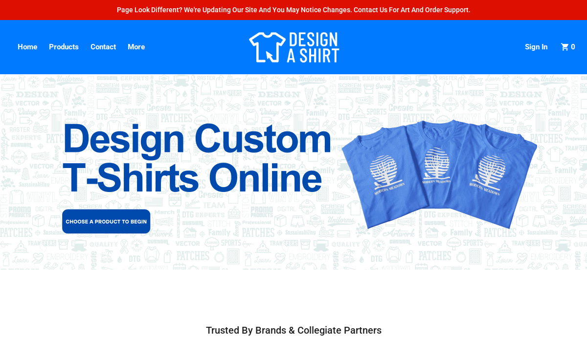 Screenshot of DesignAShirt homepage with a banner saying the site is being updated. The page offers custom T-shirt design, shows three blue T-shirts, and features navigation for Home, Products, Contact, and more.
