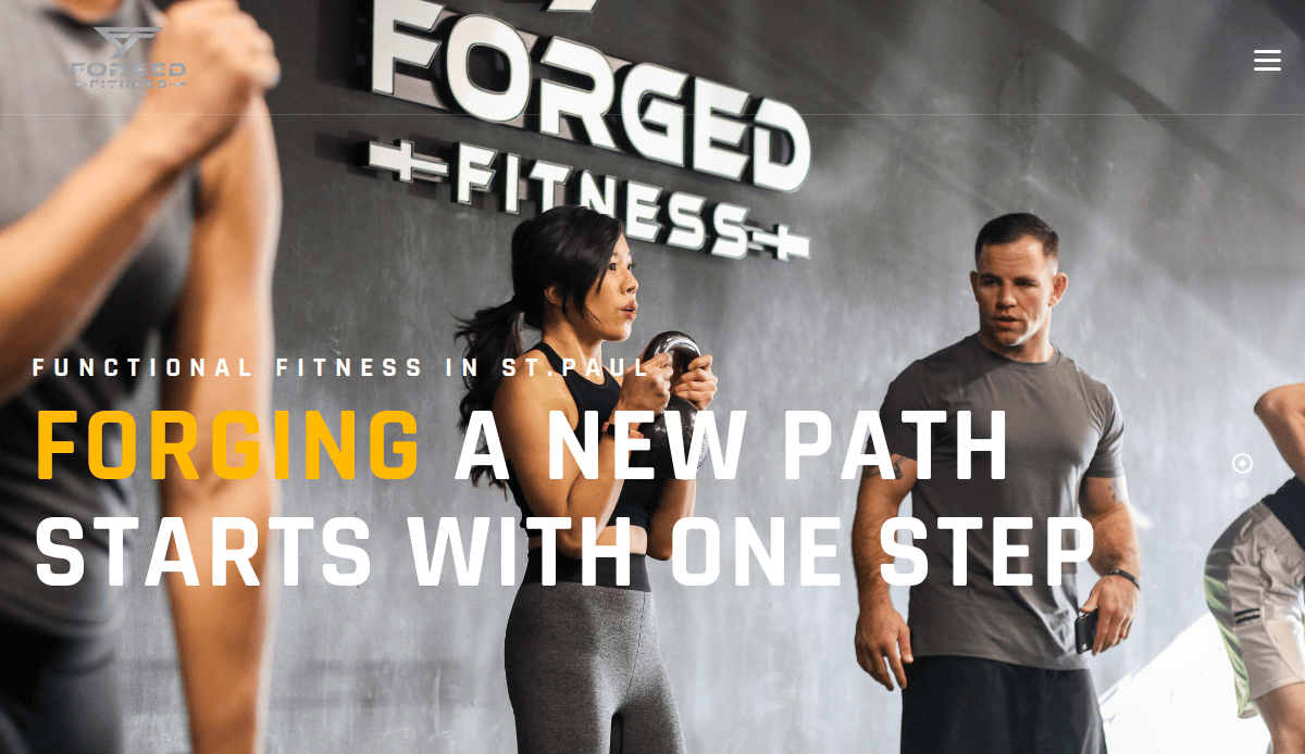 People exercising in a gym with Forged Fitness logo on the wall; large text reads “Forging a new path starts with one step.” A woman holds a kettlebell, while men stand and listen.
