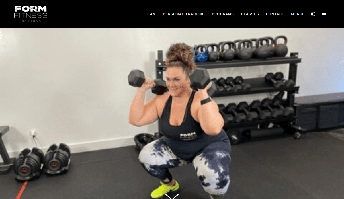 A woman in athletic wear performs a squat while holding dumbbells indoors at a gym, with kettlebells and weights on racks behind her. The wall displays the logo FORM FITNESS BROOKLYN.