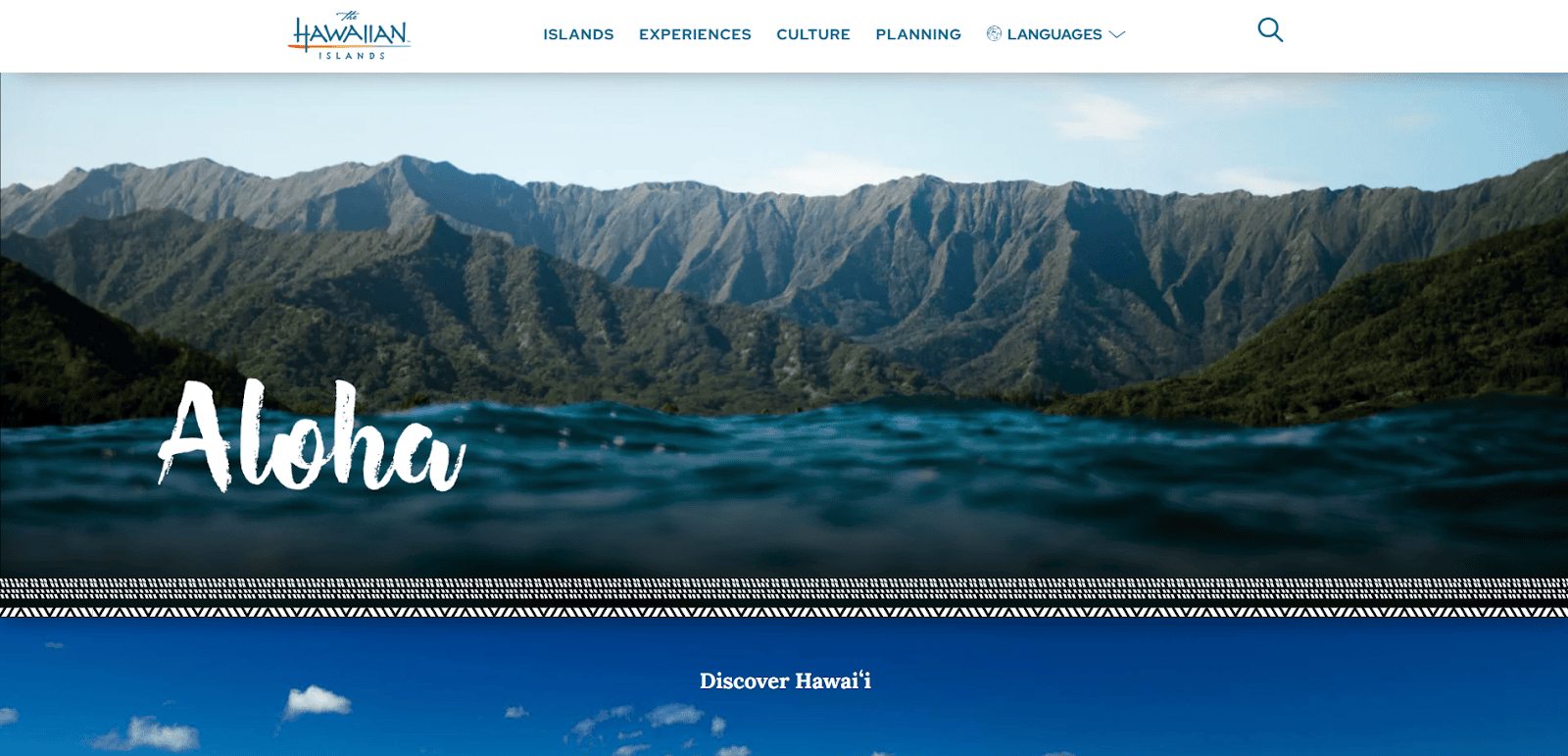 A scenic view of lush, green Hawaiian mountains with the word “Aloha” in white script over blue ocean water, from a tourism website promoting Hawaii.