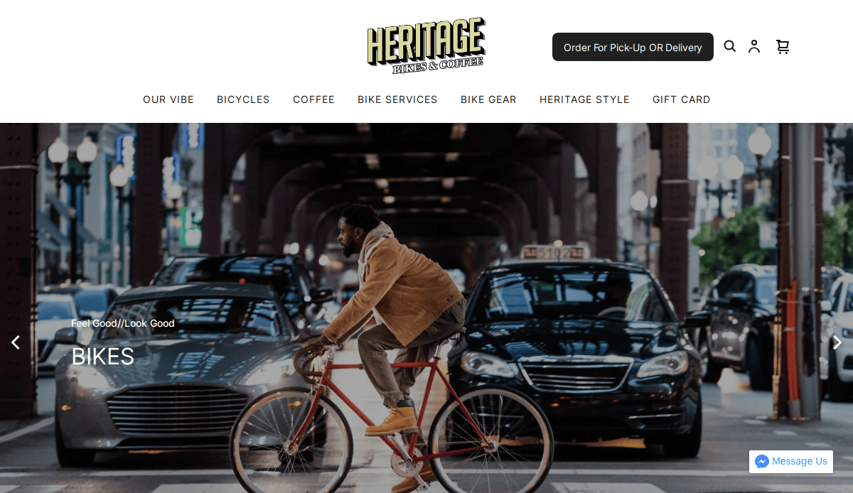 A man rides a red bicycle on a city street under an elevated train track, surrounded by cars. The website header reads Heritage Bikes & Coffee with navigation links and a coffee shop logo.