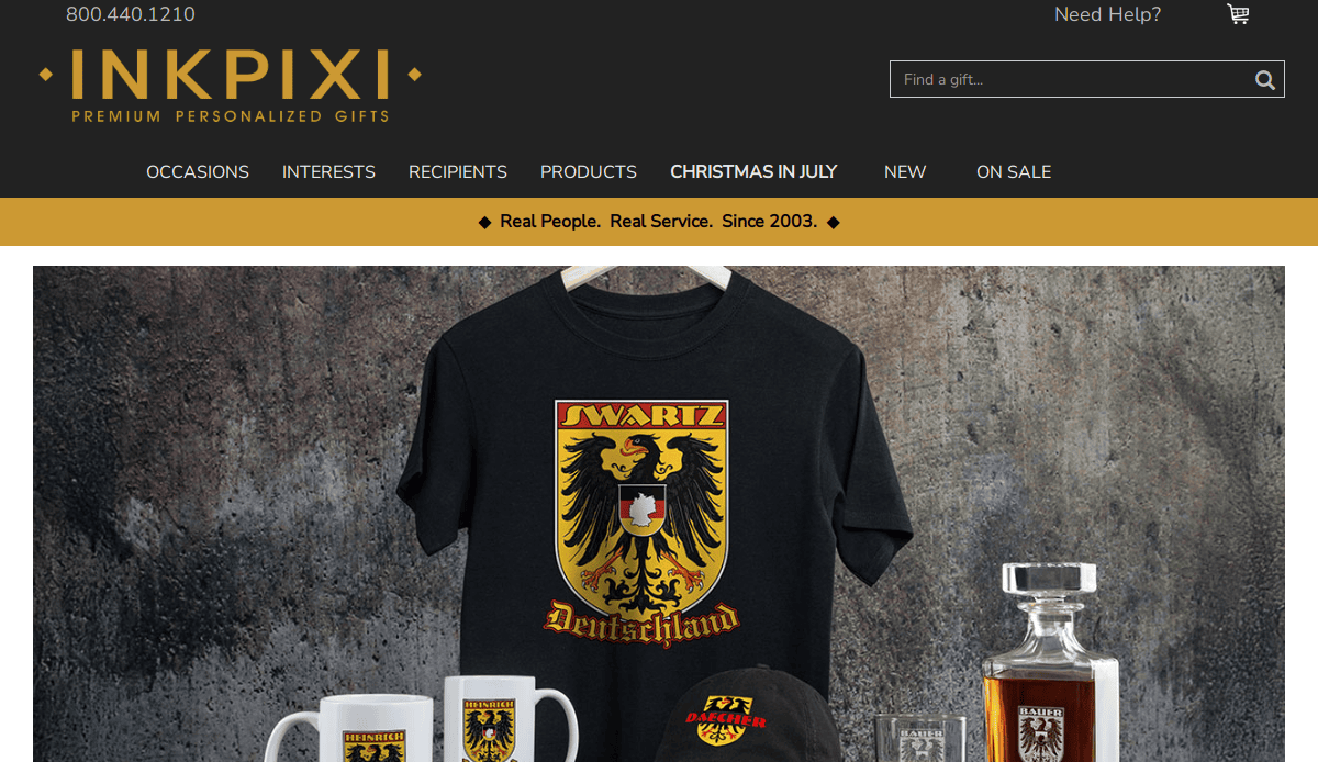Display of personalized gifts on InkPixi’s website, featuring a black Deutschland-themed t-shirt, cap, mug, and decanter, all with a yellow and red family crest. The website menu and logo appear above the product image.