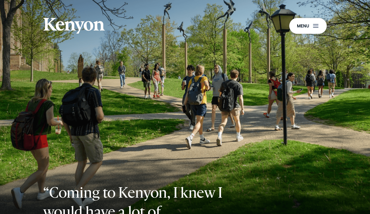 Students walk along a sunny, tree-lined campus path at Kenyon College, carrying backpacks and wearing casual clothes. A lamppost and green grass are visible, with blue sky and campus buildings in the background.
