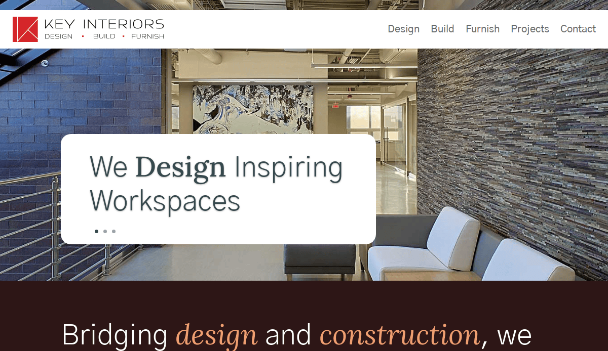 Modern office lobby with a stone accent wall, white sectional sofa, and large artwork. Text overlay reads: We Design Inspiring Workspaces. Key Interiors branding is visible at the top.