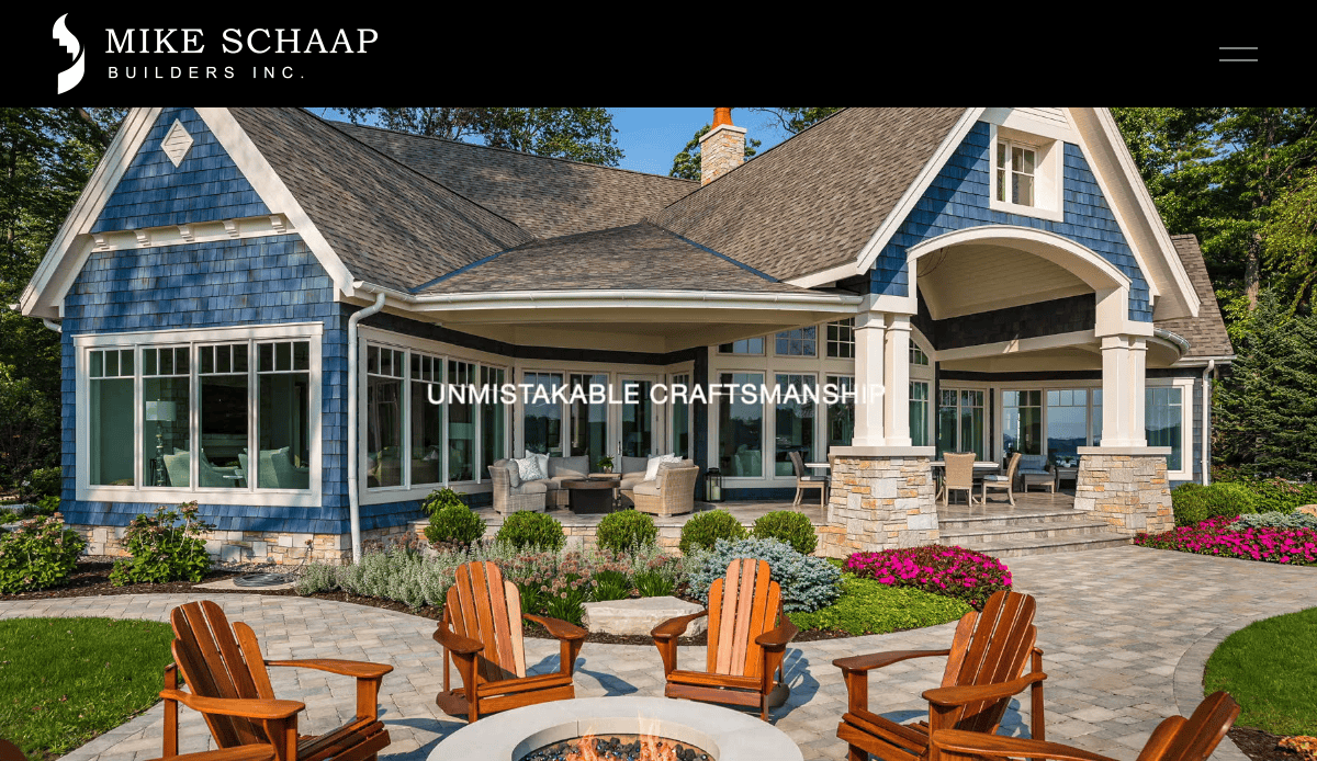 A large blue house with white trim and a covered porch, surrounded by a stone patio, green lawn, and Adirondack chairs around a fire pit. The text UNMISTAKABLE CRAFTSMANSHIP is centered on the image.