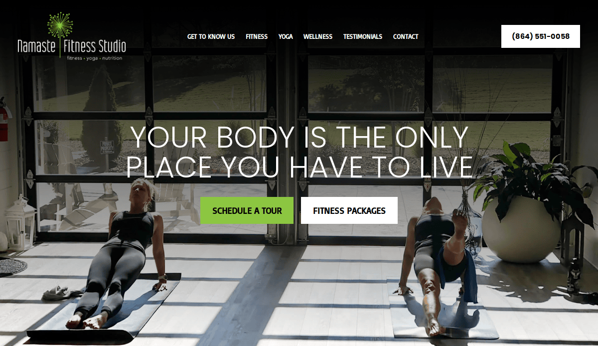 Two women in athletic wear exercise on yoga mats in a sunlit studio. Large windows let in natural light. Overlaid text reads, Your body is the only place you have to live. Studio menu and contact info are visible.