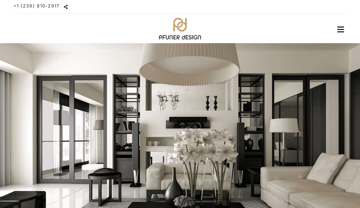 A modern living room with neutral tones, featuring a beige sofa, black shelves, a large round light fixture, and a coffee table with white flowers. Large windows let in natural light.