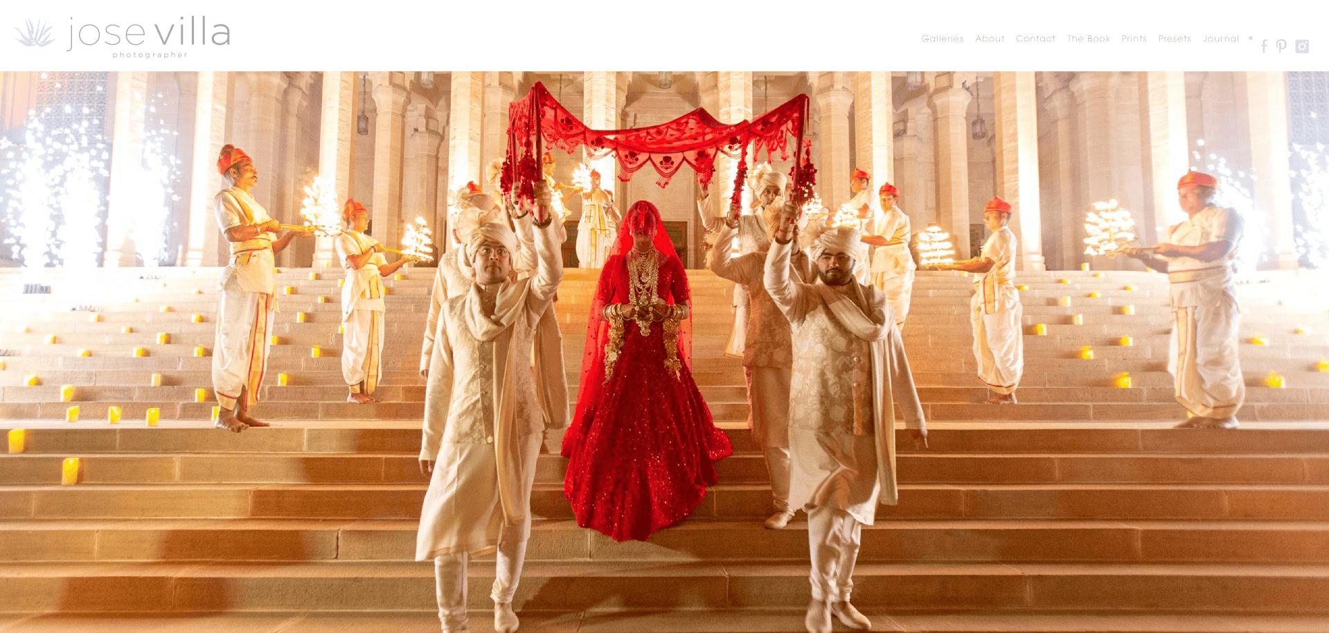 A bride in a red dress walks down steps flanked by men in white traditional attire holding candle stands, beneath an ornate red canopy—an inspiring scene for photography website design, showcasing one of the best examples of visual storytelling.