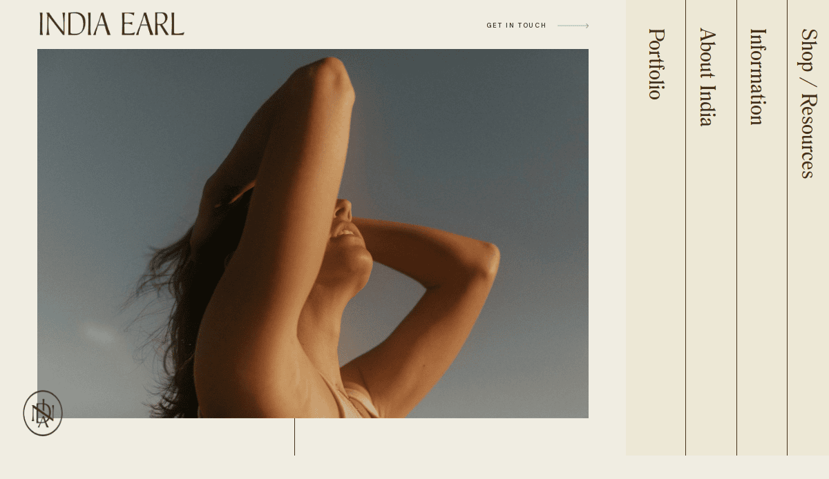 A woman stands outdoors with her arms raised behind her head, looking up and smiling softly. The clear blue sky sets a serene mood, ideal for a photography website design featuring menu text and the name India Earl on a beige background.