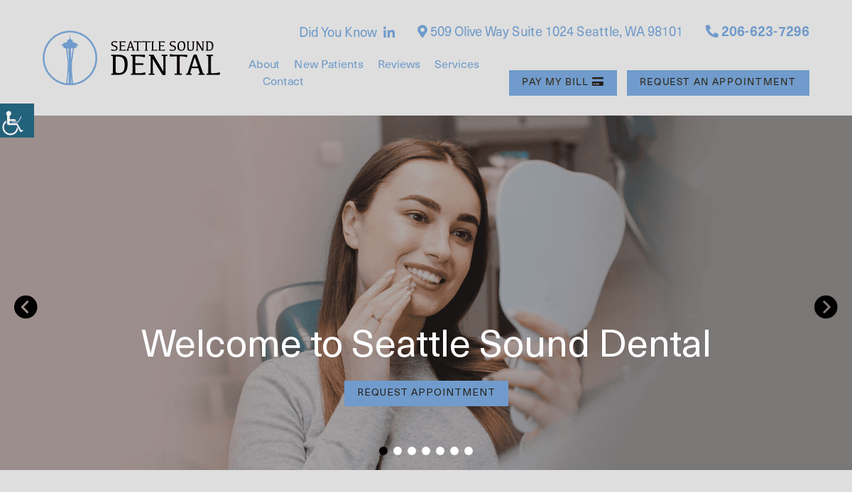 A woman smiles while looking into a handheld mirror at a dental clinic. The screen shows the Seattle Sound Dental website, displaying contact info, navigation menu, and a welcome message.