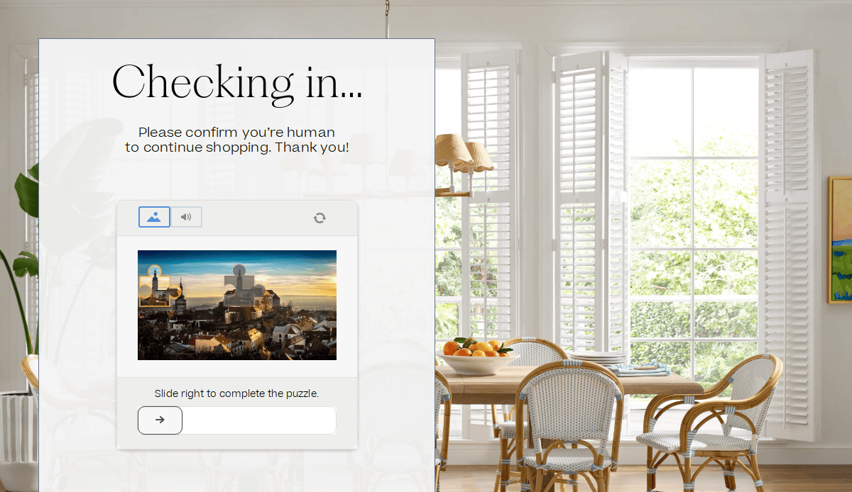 A website pop-up asks users to complete a puzzle to confirm they are human. The background shows a sunlit dining room with a wooden table, chairs, fruit bowl, and large windows with white shutters.
