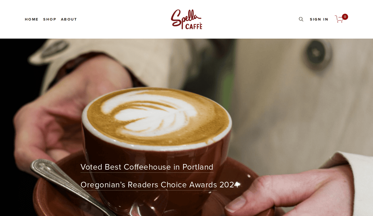 Close-up of hands holding a cup of latte with foam art. Text on the image reads: Voted Best Coffeehouse in Portland, Oregonian’s Readers Choice Awards 202[cut off]. Spella Caffè logo is at the top.