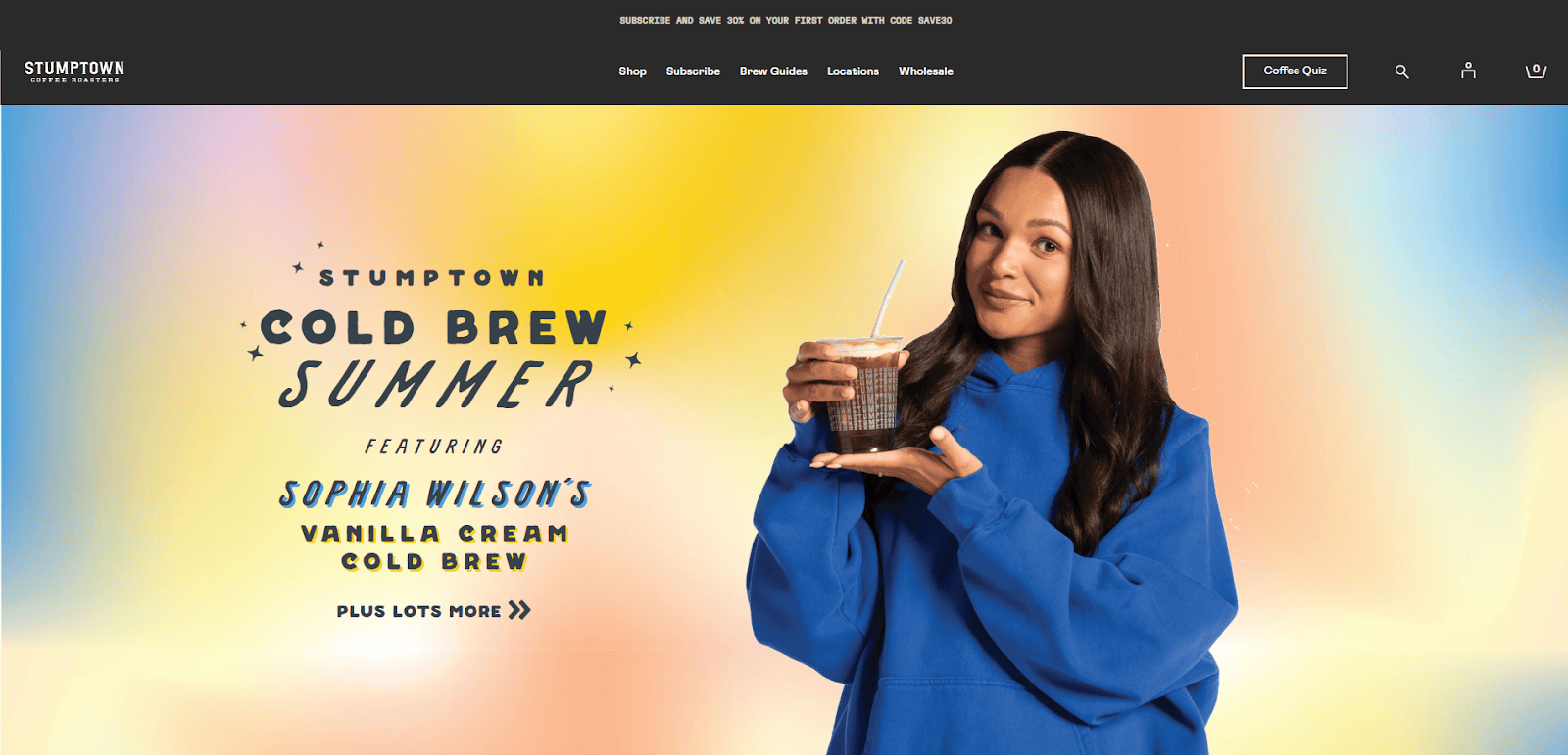 A smiling woman in a blue hoodie holds a glass of iced coffee against a pastel gradient background. Text reads: Stumptown Cold Brew Summer featuring Sophia Wilson’s Vanilla Cream Cold Brew.