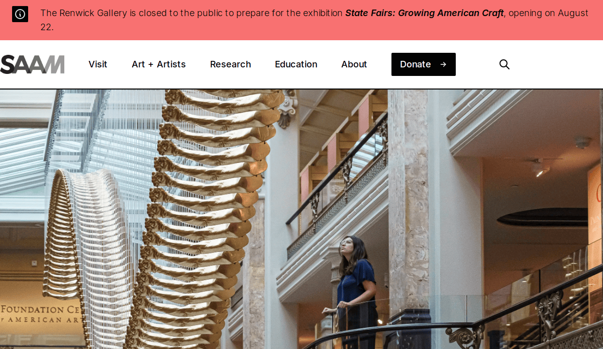 A woman stands on a balcony beside a large dinosaur skeleton hanging from the ceiling at the Smithsonian American Art Museum. A red banner at the top announces the closure of the Renwick Gallery for an upcoming exhibition.