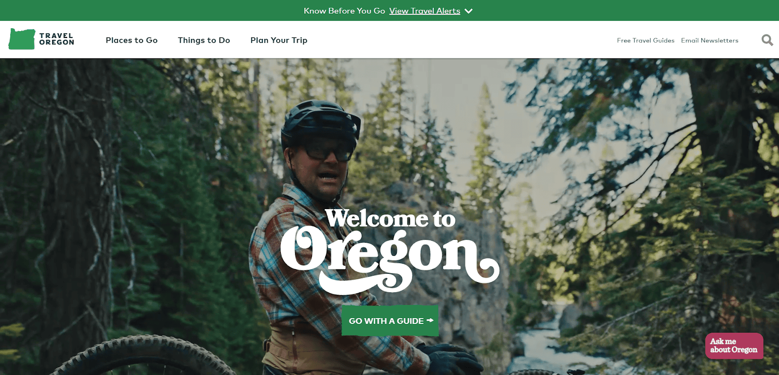 A person wearing a helmet and plaid shirt sits on a mountain bike in a forested Oregon landscape with “Welcome to Oregon” text overlaid and website navigation menu at the top.
