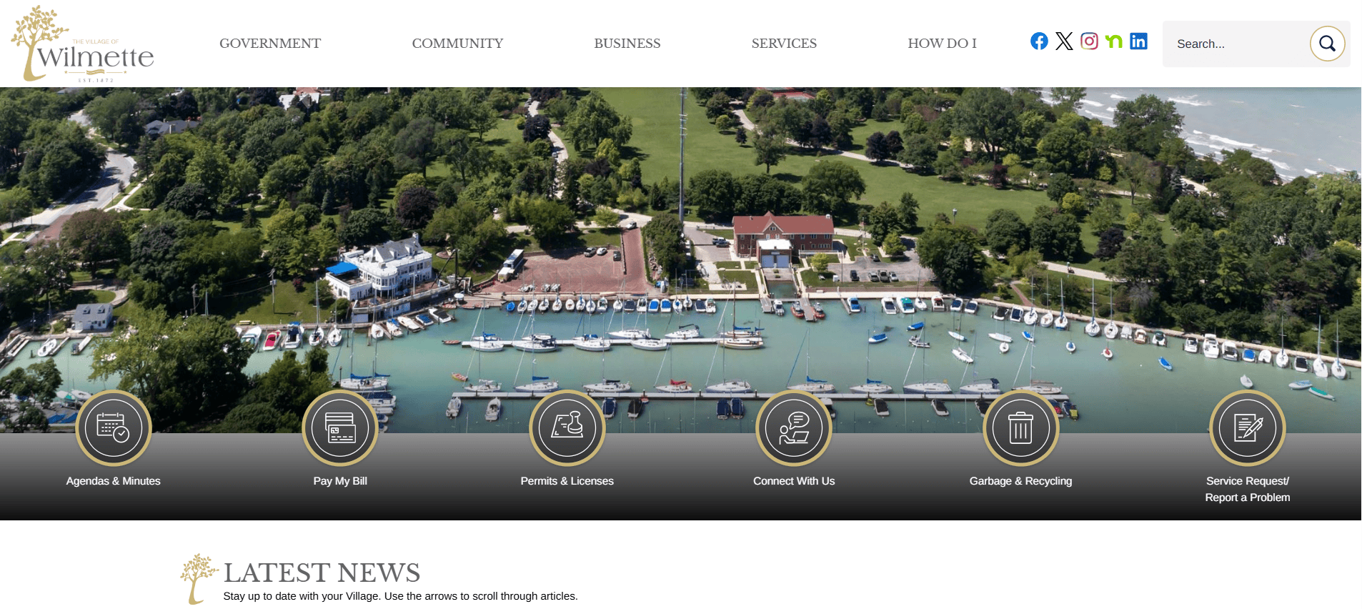 Aerial view of a marina with many boats docked, surrounded by green trees and buildings. The website header reads “Village of Wilmette.” Navigation and news sections are visible on the page.