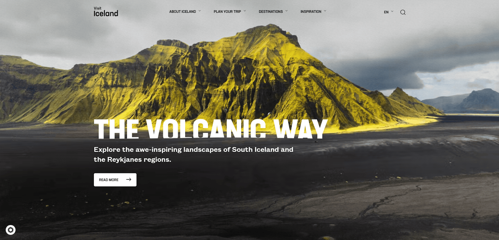 A dramatic yellow-green moss-covered volcanic mountain rises under a cloudy sky in Iceland. White text overlay reads: THE VOLCANIC WAY. Explore the awe-inspiring landscapes of South Iceland and the Reykjanes regions.