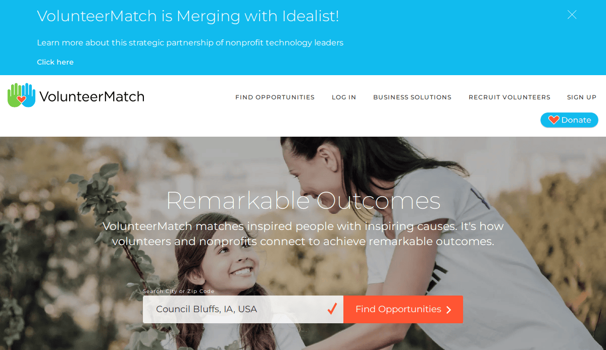 Screenshot of the VolunteerMatch homepage showing a banner about its merger with Idealist, the VolunteerMatch logo, a search bar for finding volunteer opportunities, and a photo of a smiling woman and child.