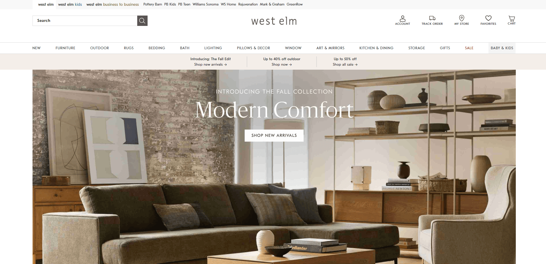 West Elm website homepage featuring a modern living room with a gray sofa, wooden coffee table, and shelves with decor. The banner text reads Introducing the Fall Collection: Modern Comfort. Shop New Arrivals.