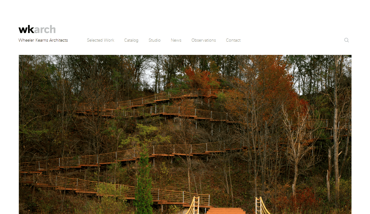 A series of wooden stairs and walkways zigzag up a wooded hillside with autumn trees, viewed from the base looking upward.