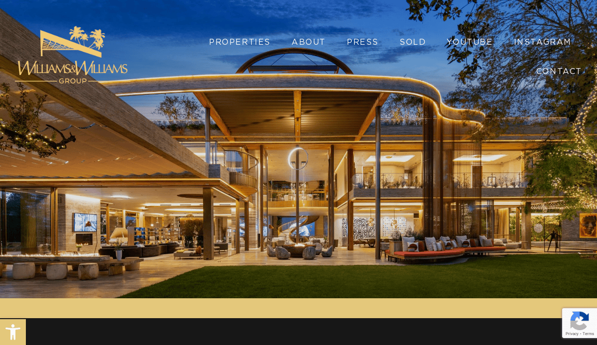 Modern luxury mansion with large glass walls, stylish lighting, and open patio seating at dusk. The Williams & Williams Group logo is in the top left, and navigation links are at the top of the webpage.
