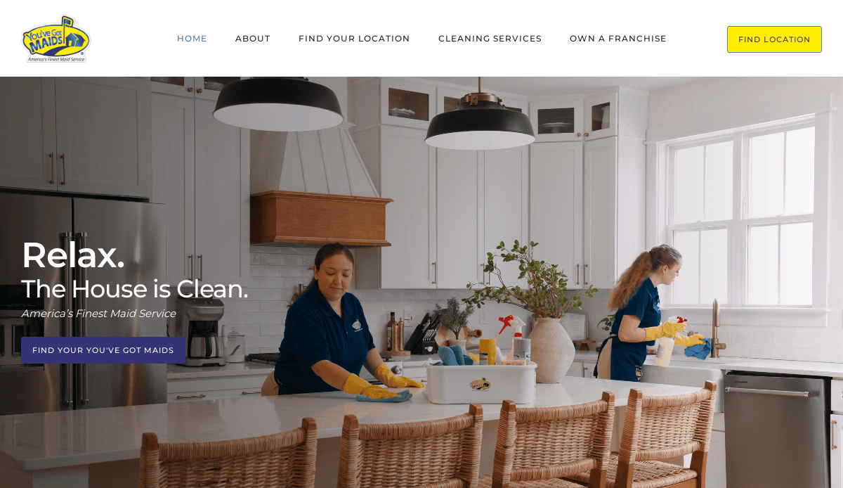 Two professional cleaners in blue uniforms and yellow gloves clean a bright, modern kitchen with white cabinets and countertops. One wipes the counter while the other cleans near the sink. Text overlay promotes maid services.